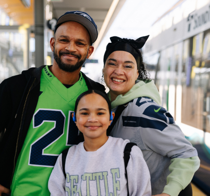 A family wearing Seattle sports gear pose for a photo at a Link station.